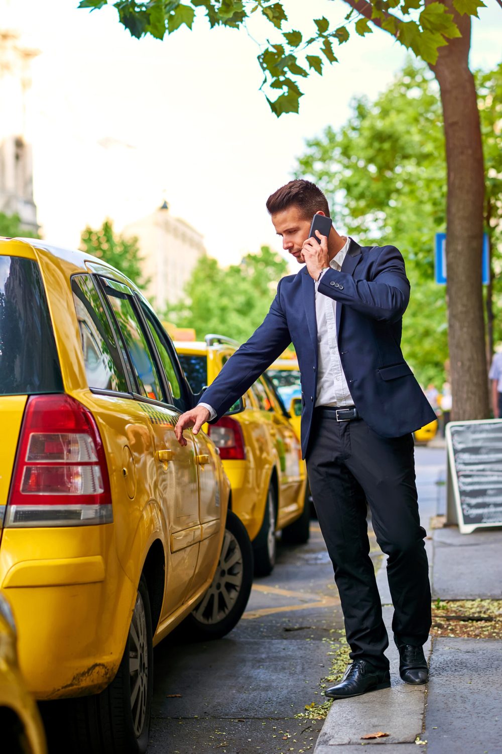 A handsome young businessman walking to a taxi on the street while talking on his phone